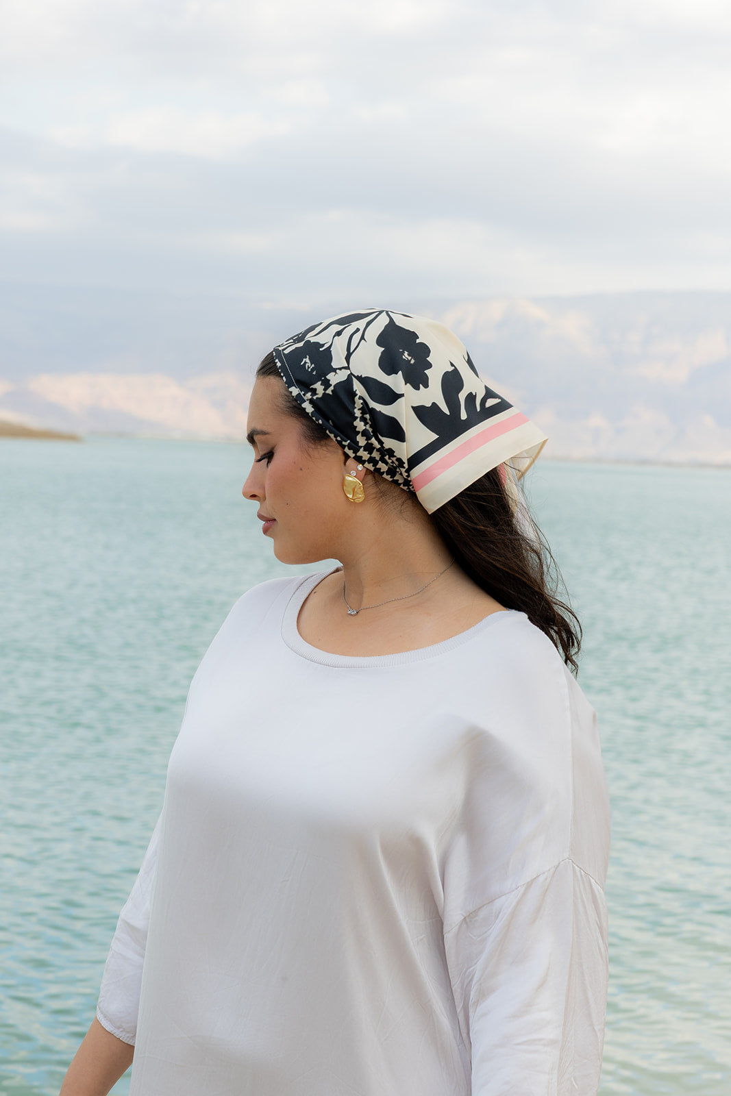 TUK Checked Out Silk Bandana worn seaside with a white outfit, featuring a black floral print silk bandana design.