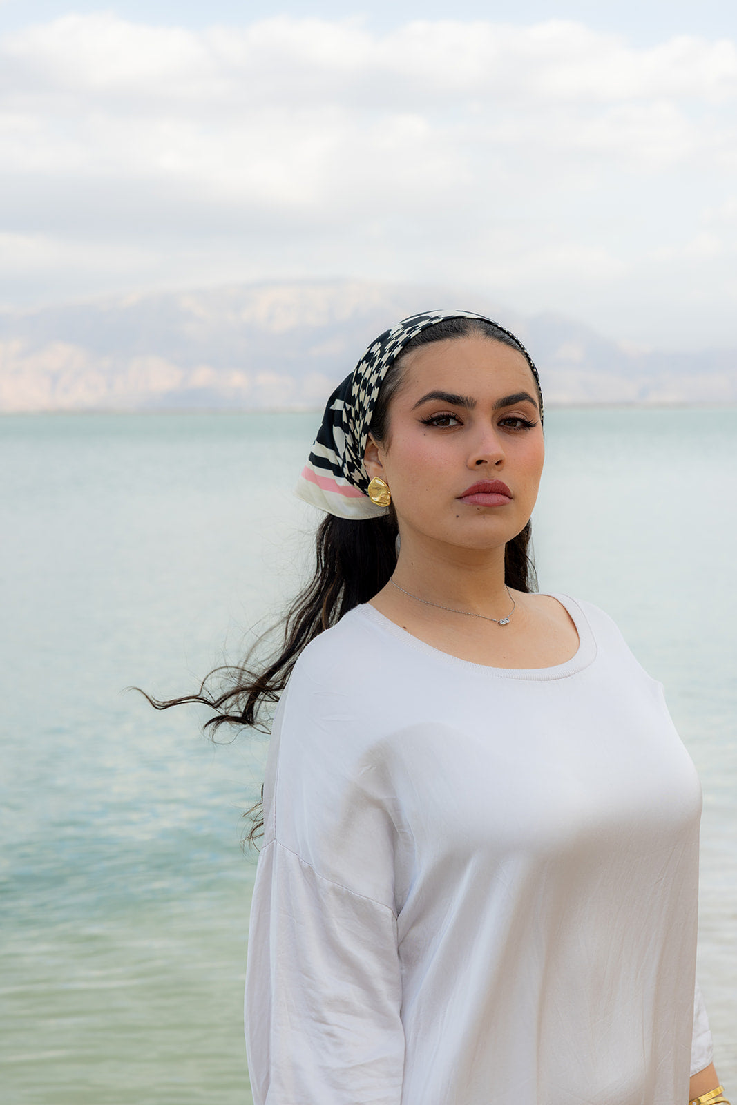 TUK Checked Out Silk Bandana styled with a white outfit by the sea, featuring a black and cream check silk bandana print.