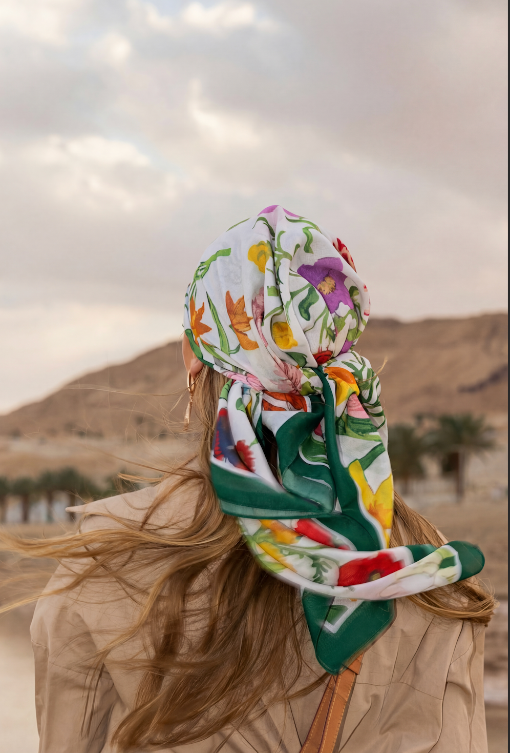 Person wearing a colorful floral headscarf with a desert landscape in the background.