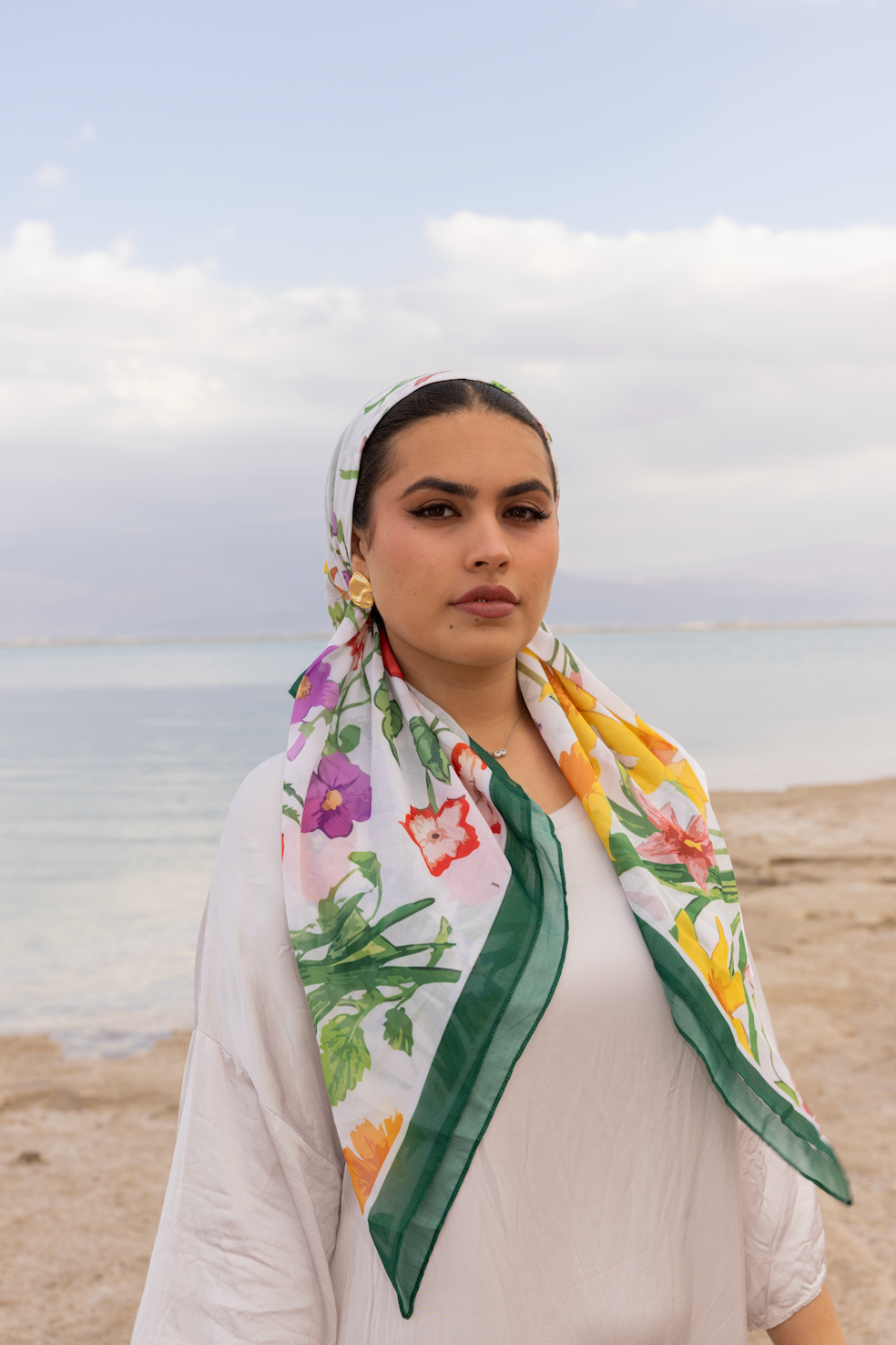 Woman wearing a colorful floral headscarf on a beach.