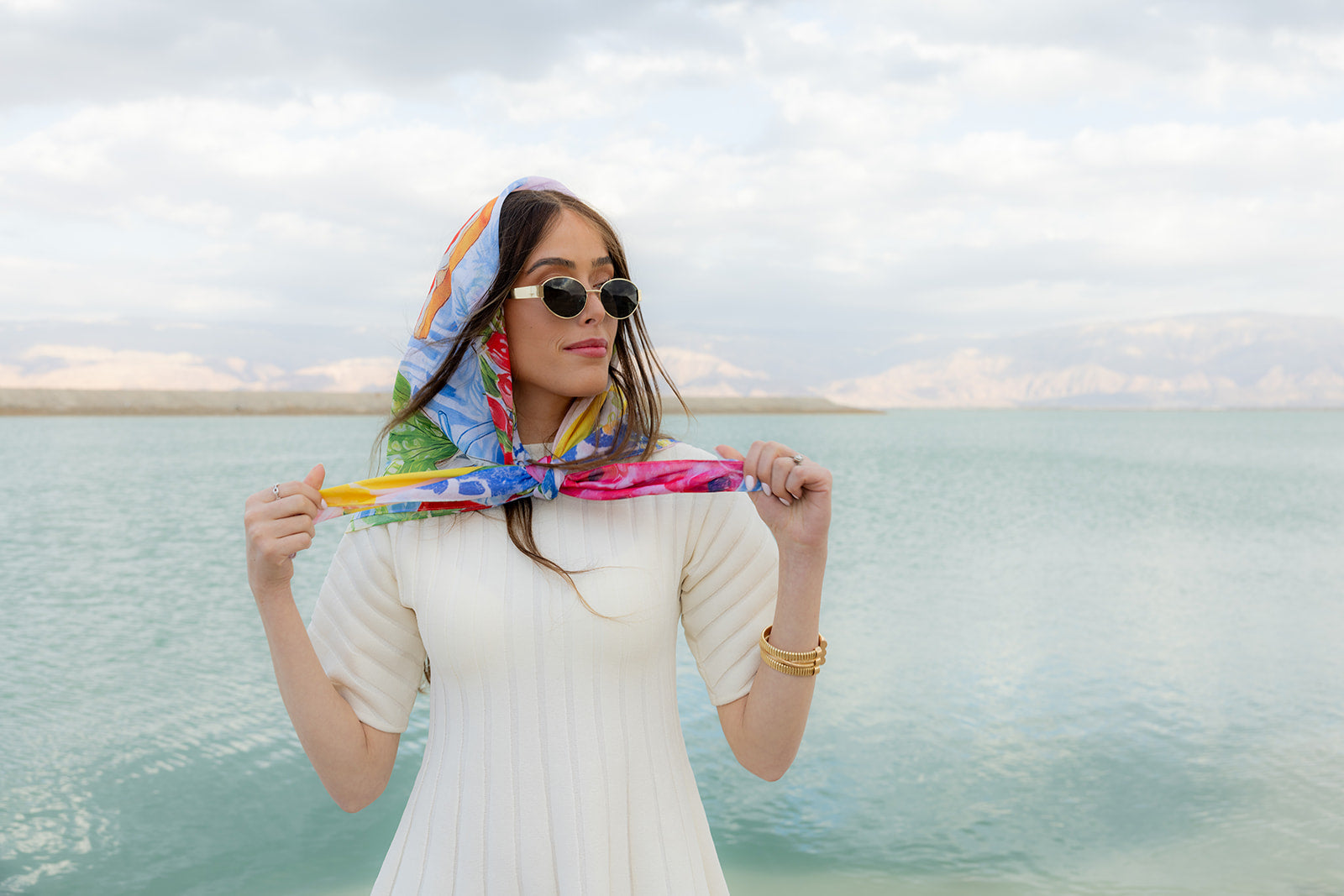 TUK Fleurs & Citrons Silk Bandana with vibrant floral and citrus print styled as a headscarf by a serene waterfront.