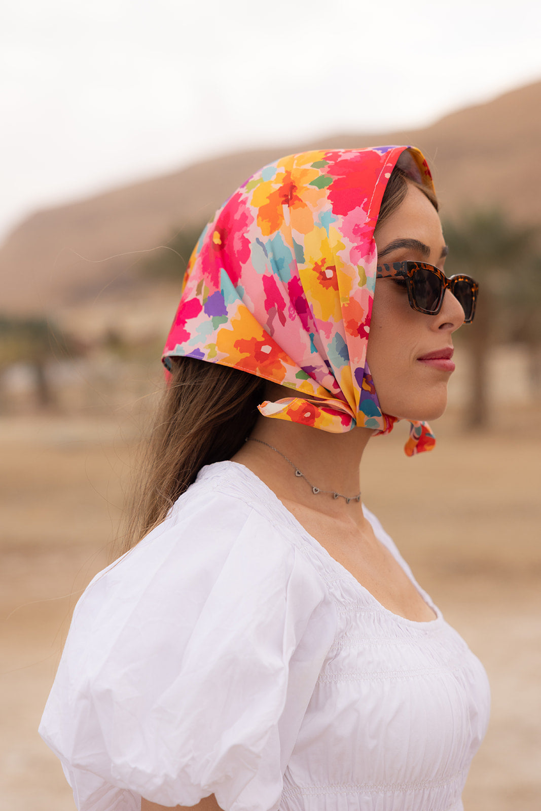 TUK Flower Hour Silk Bandana in vibrant floral print styled as a chic headscarf with sunglasses and a white blouse outdoors.