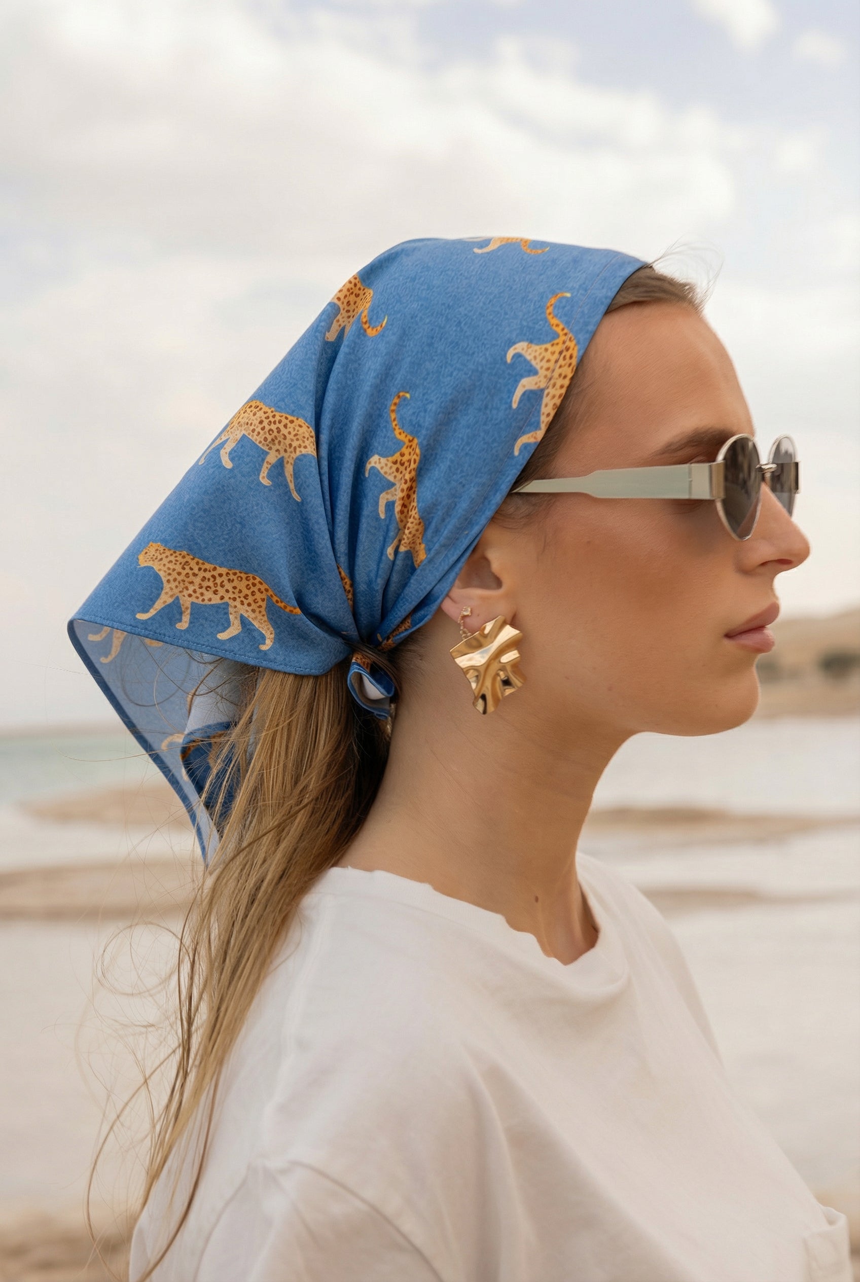 Woman styling TUK Haute Pursuit Silk Scarf crochet bandana in blue cheetah print with chic beachwear look.
