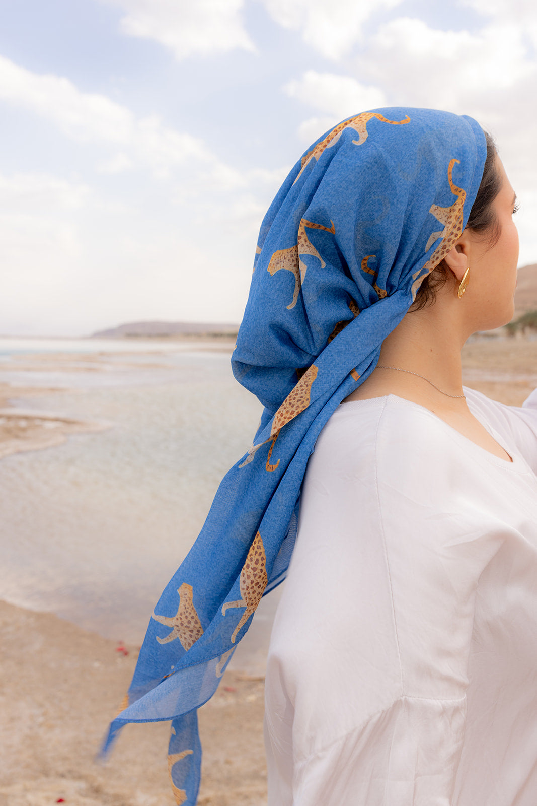 Haute Pursuit Head Scarf by TUK in bold blue with golden leopard print, styled as a chic head wrap by the shoreline.