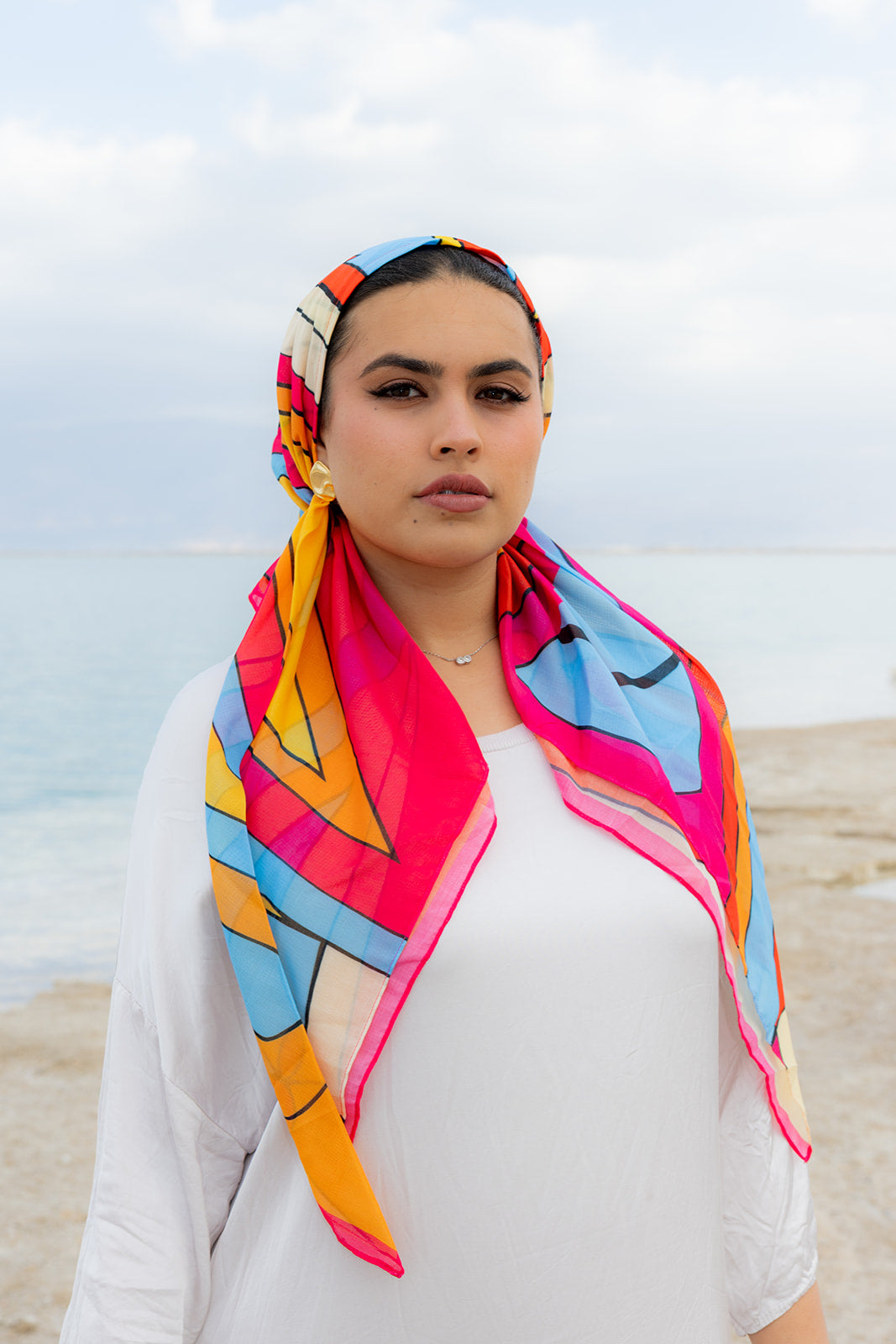 Hot Line Head Scarf by Tie Ur Knot featuring a vibrant geometric print in pink, orange and blue, styled by the waterfront.