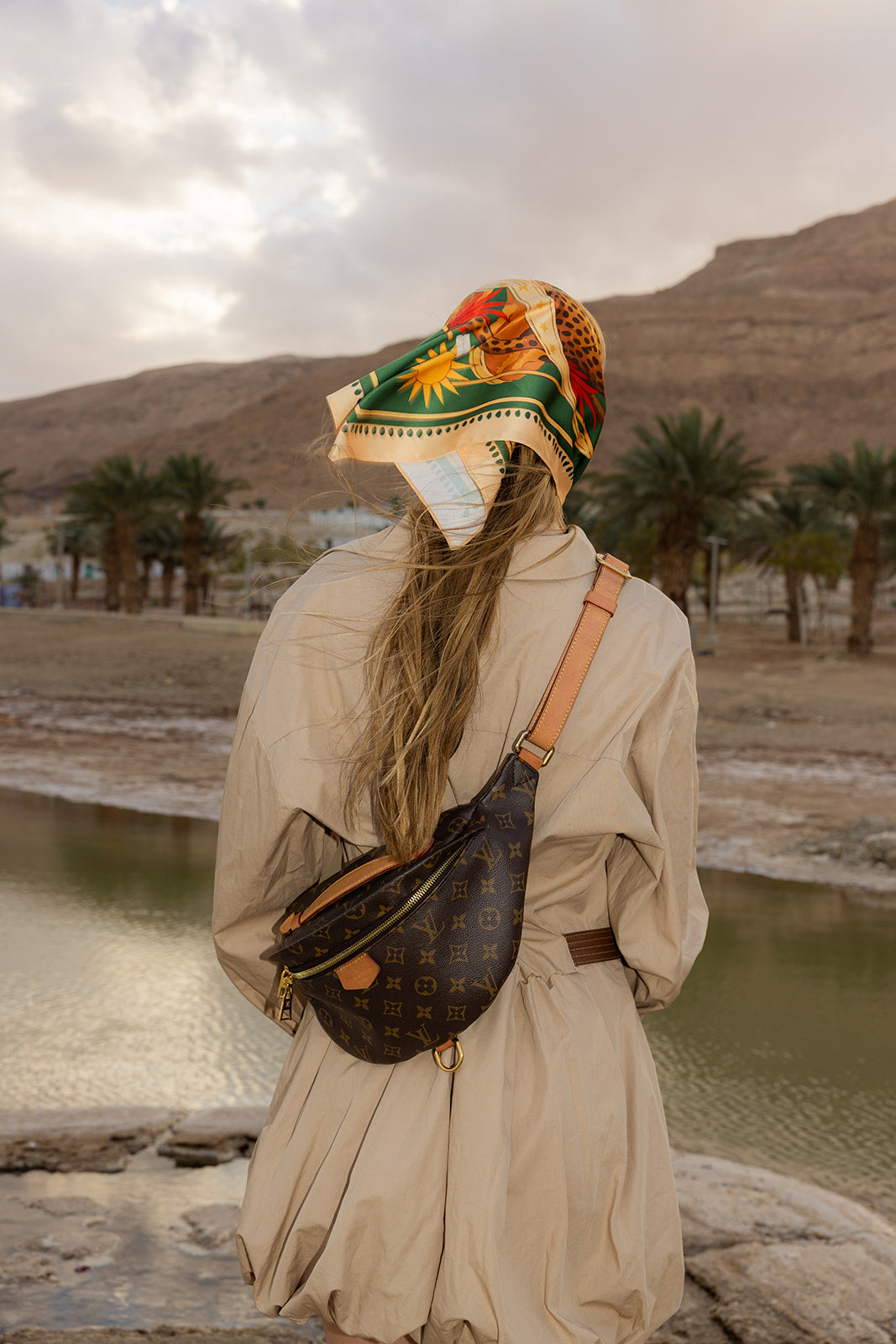 TUK Knot So Tame Silk Bandana with bold safari print worn as a headscarf, adding luxury style to a scenic desert landscape.