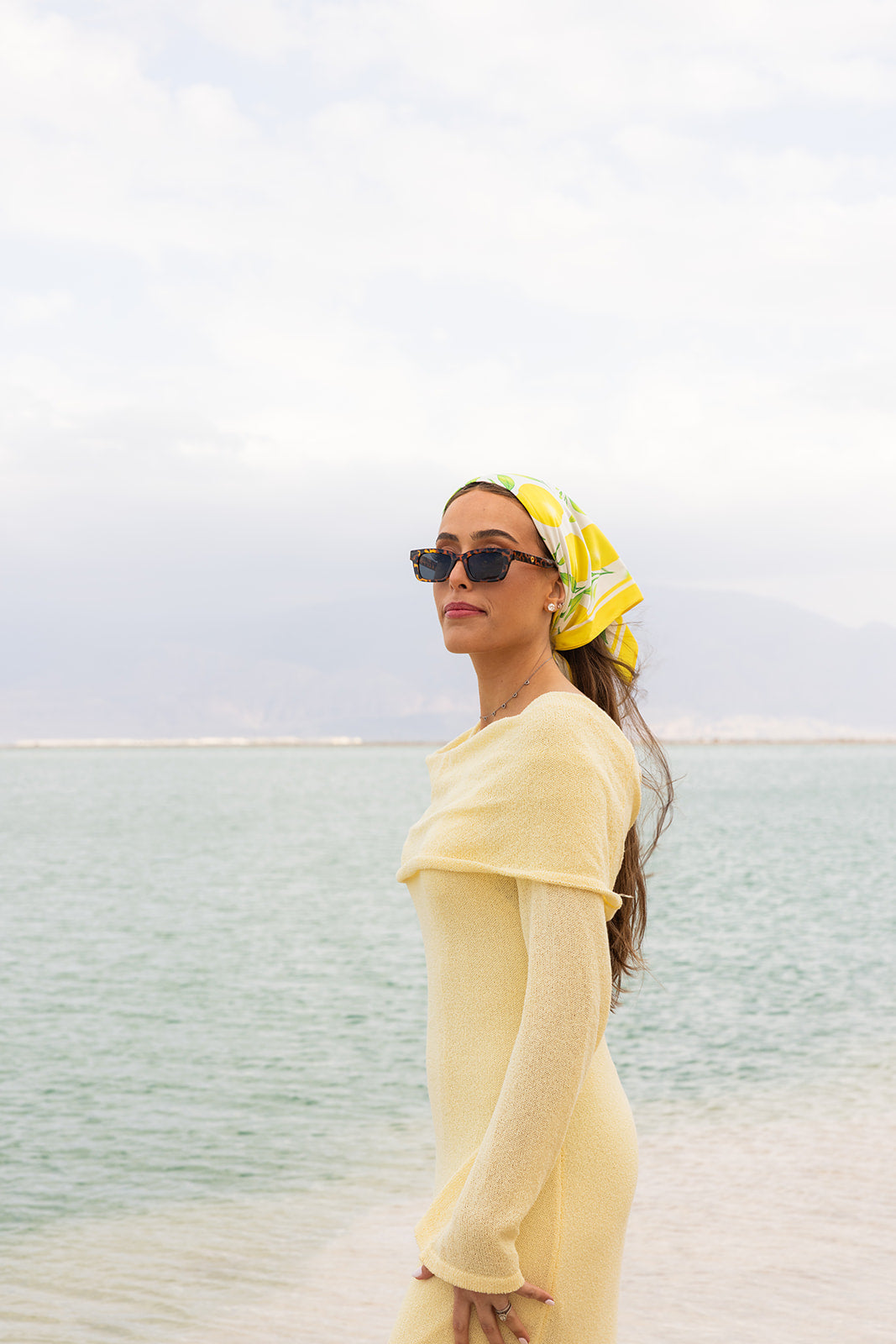 La Limonaia Silk Bandana by TUK with vibrant lemon print, styled as a headscarf for an elegant coastal summer look.