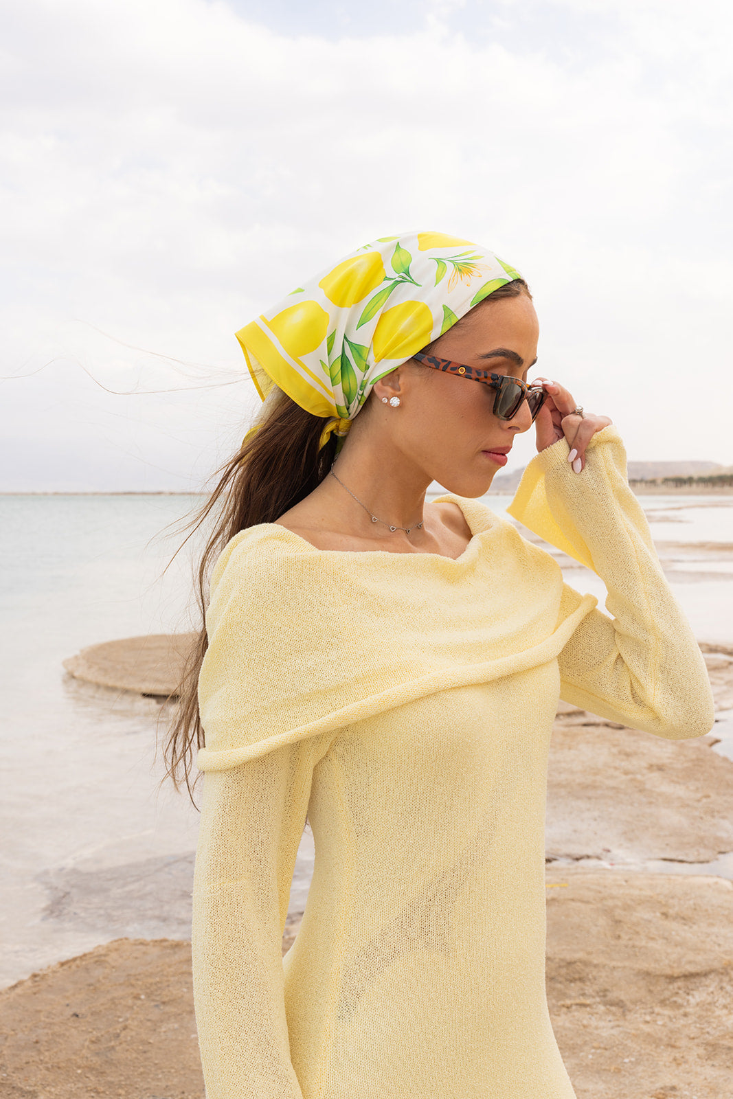 La Limonaia Silk Bandana by TUK featuring vibrant lemon print, styled seaside with elegant resortwear for a chic summer look.