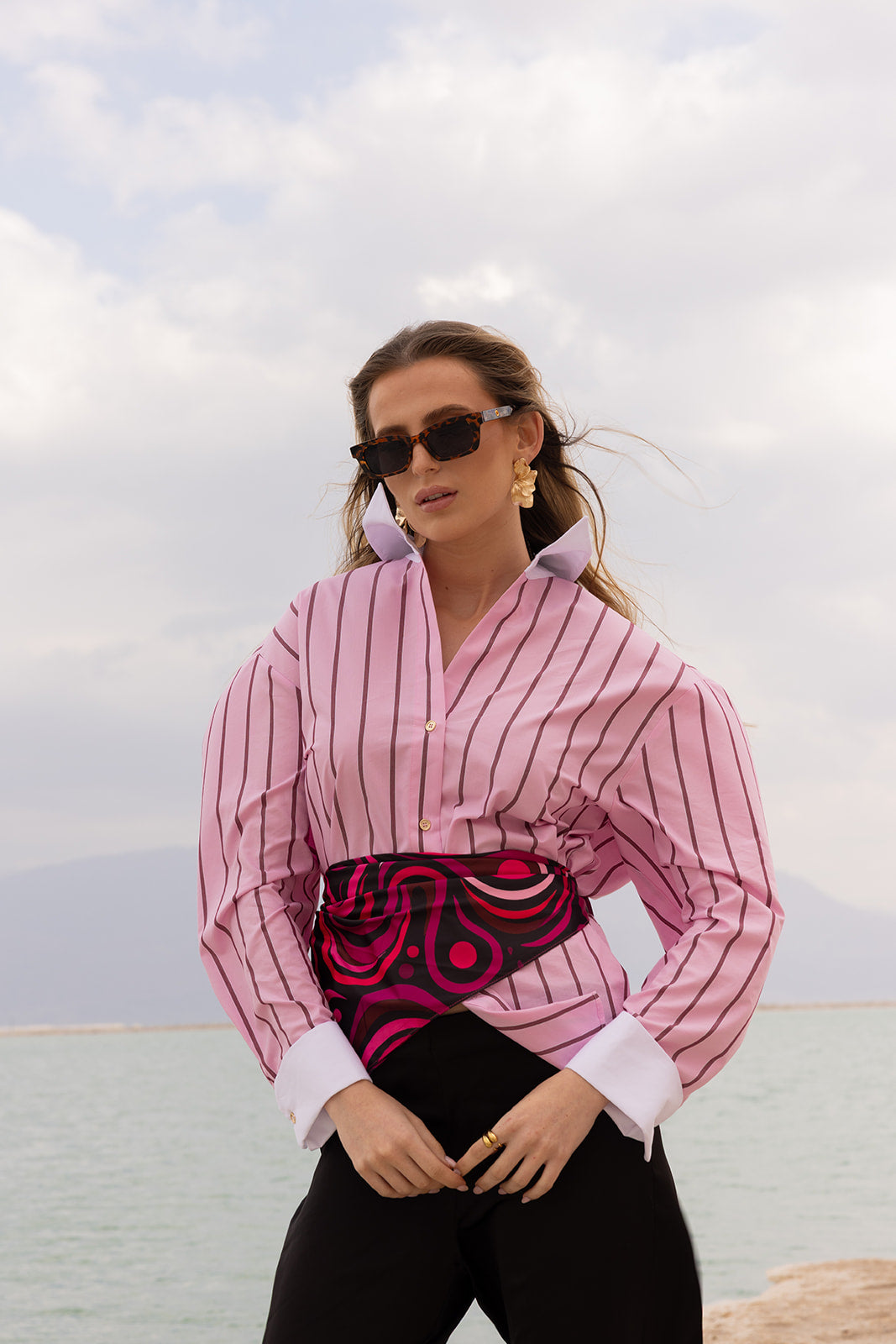 Mind Over Matter Silk Bandana styled as a bold waist sash with a pink striped shirt, creating a chic statement look.