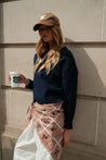 Model wearing TUK’s Neutral Position headscarf styled over white pants, paired with navy sweater and tan cap, street look.