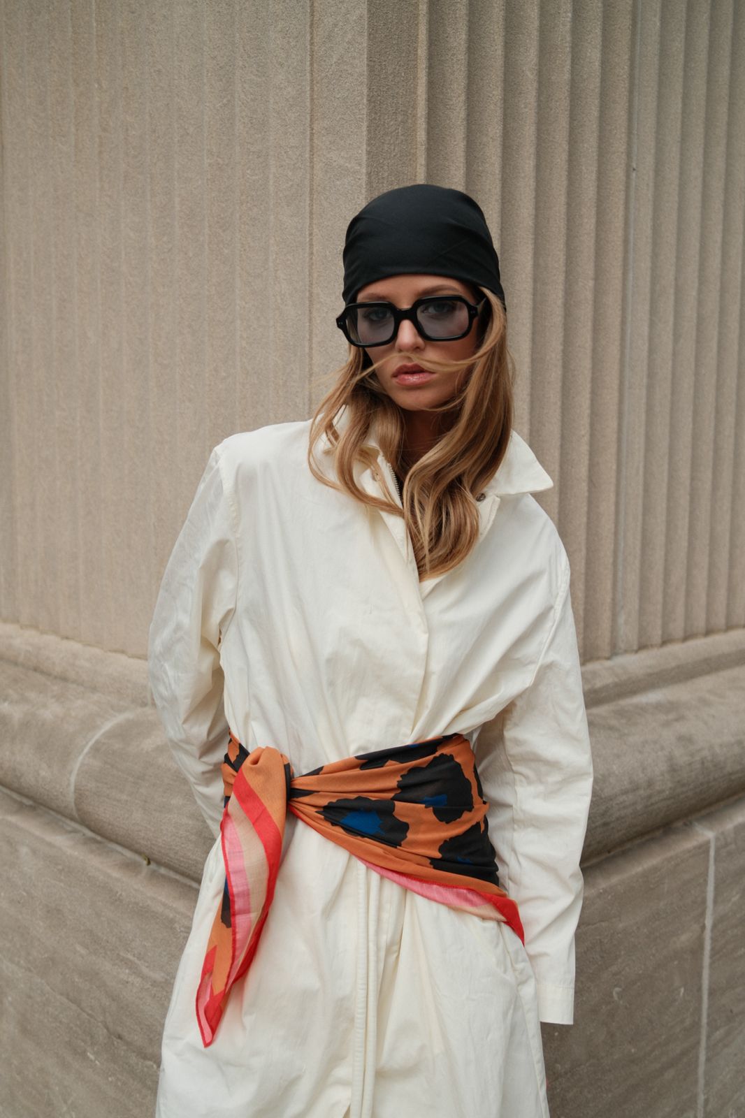 Model wearing TUK’s Out Of Line headscarf styled as belt over white dress, paired with black head wrap and sunglasses.
