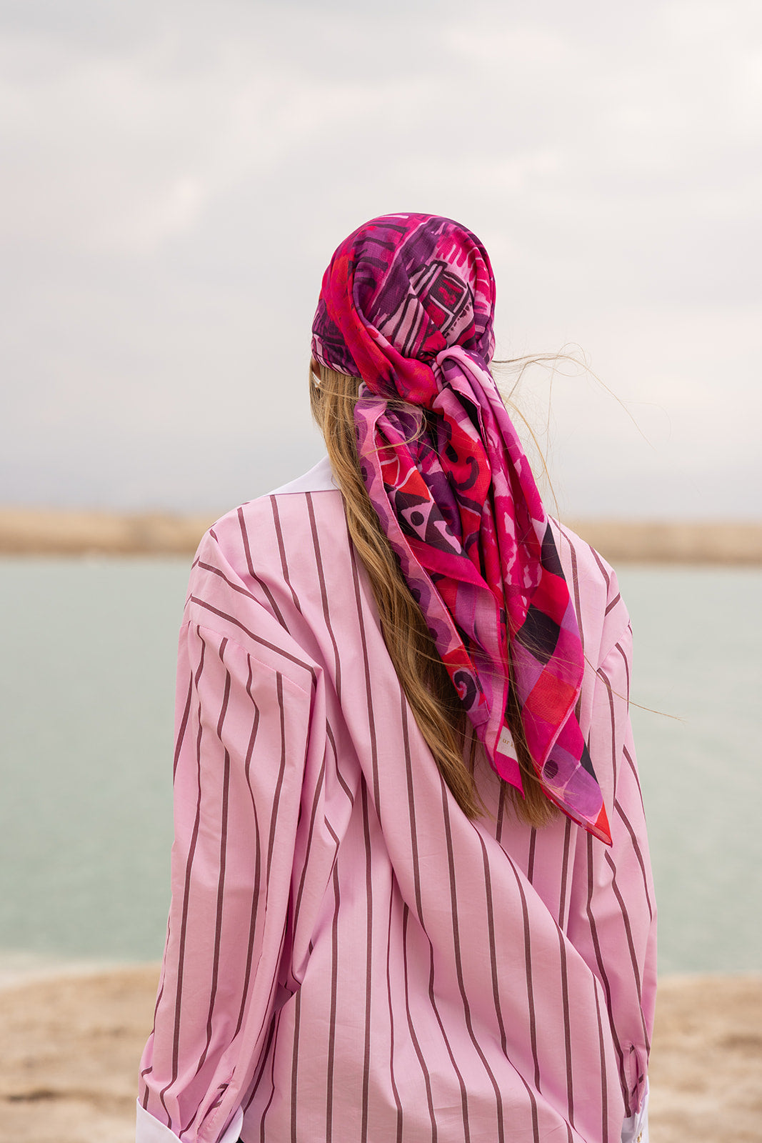Pardon My French Head Scarf by TUK in vibrant pink print, styled over long hair with a striped blouse by the water.