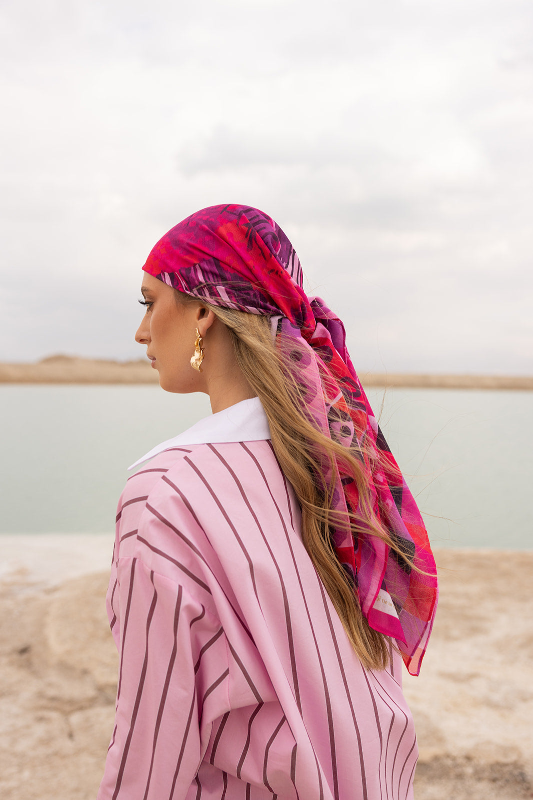 Pardon My French Head Scarf by TUK in bold pink and magenta print, elegantly styled with flowing hair by the shore.