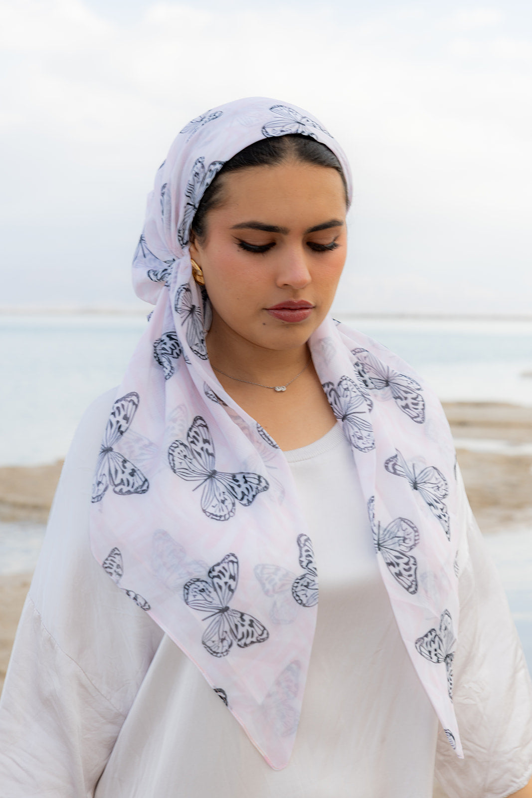 Pink Haze Head Scarf by TUK featuring delicate butterfly prints on soft blush fabric, styled elegantly by the seaside.
