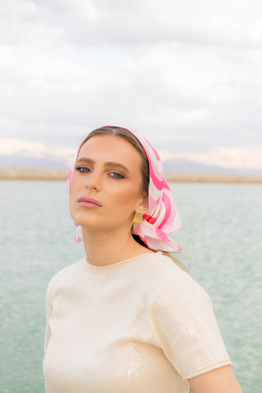Model wearing TUK Pretty In Motion Silk Bandana in pink geometric print, styled for an elegant coastal summer look.