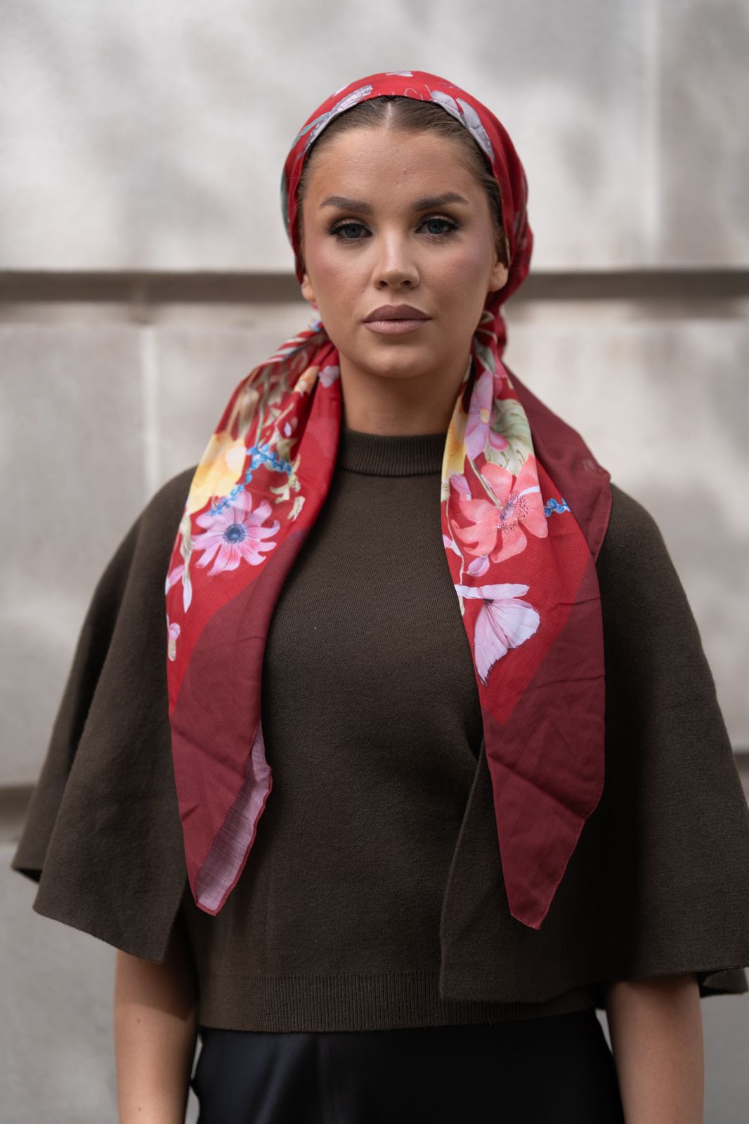 Model wearing TUK’s Redacted Pre-tied Head Scarf in rich red with vibrant floral prints, styled elegantly over dark attire.