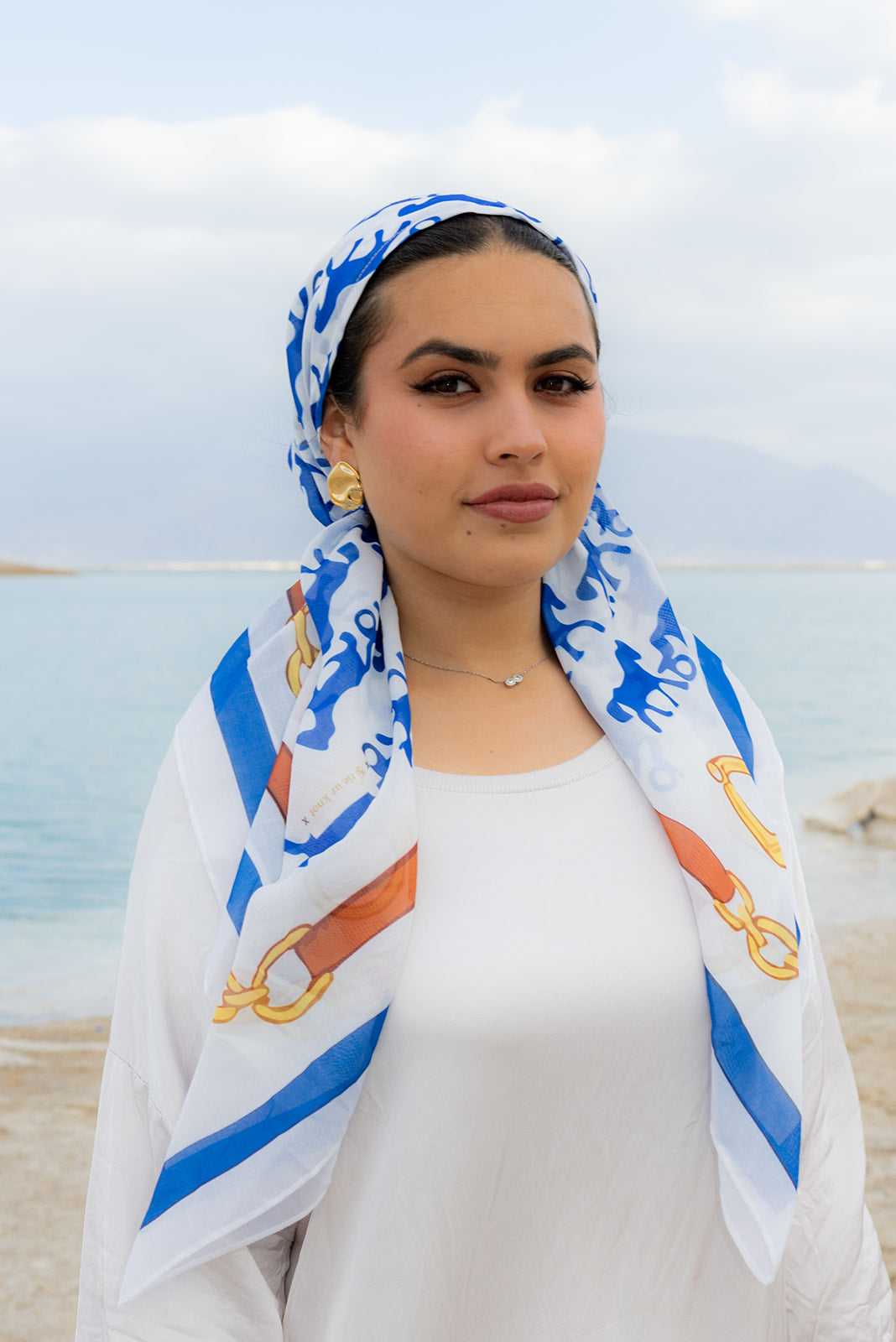 Rein It In Head Scarf by Tie Ur Knot, a chic blue and gold equestrian-inspired head scarf styled by a serene waterfront.