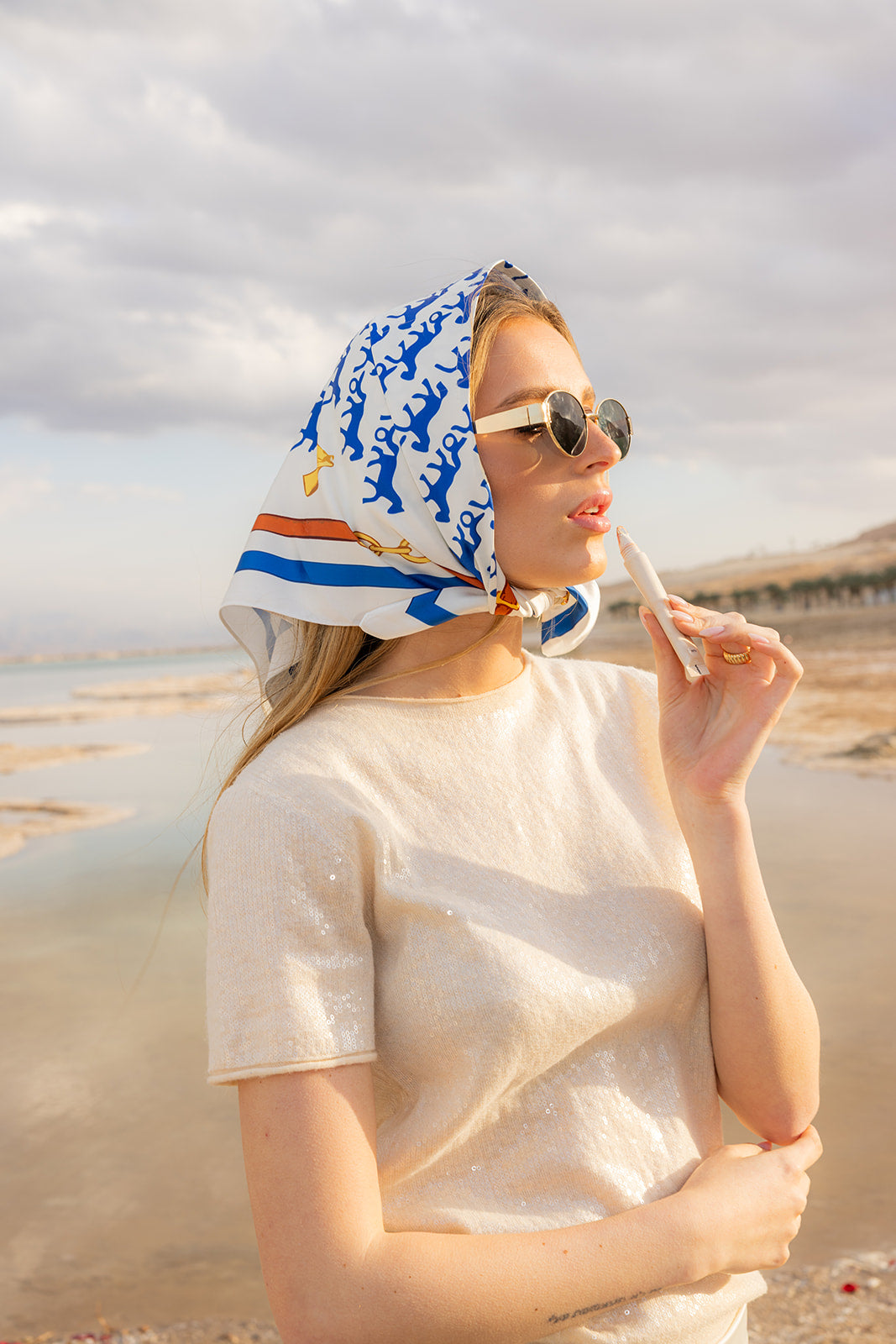Model wearing TUK Rein It In Silk Bandana with blue equestrian print, styled at the beach with a chic luxury look.