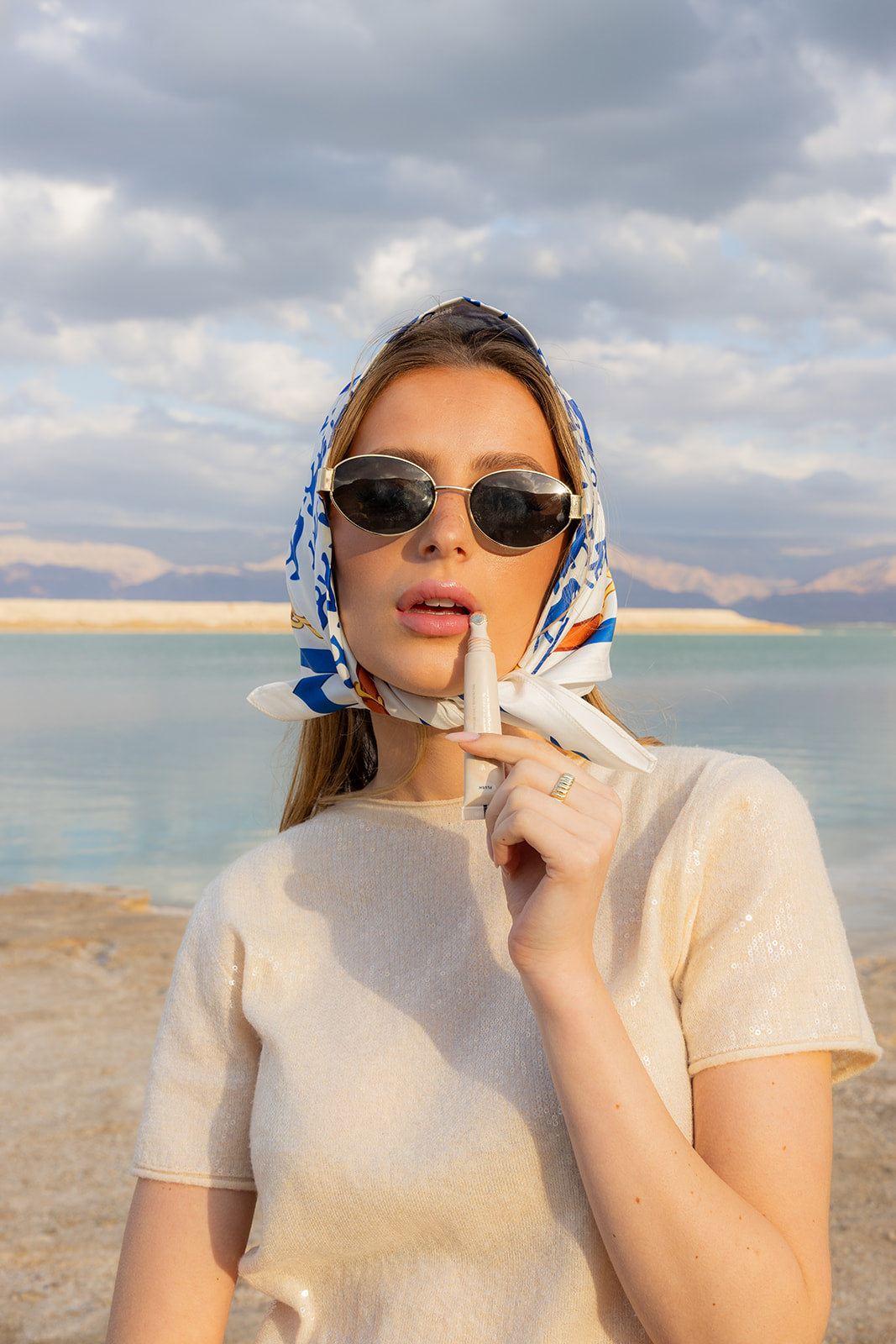 Model wearing TUK Rein It In Silk Bandana with blue equestrian print, styled with sunglasses by the beach.