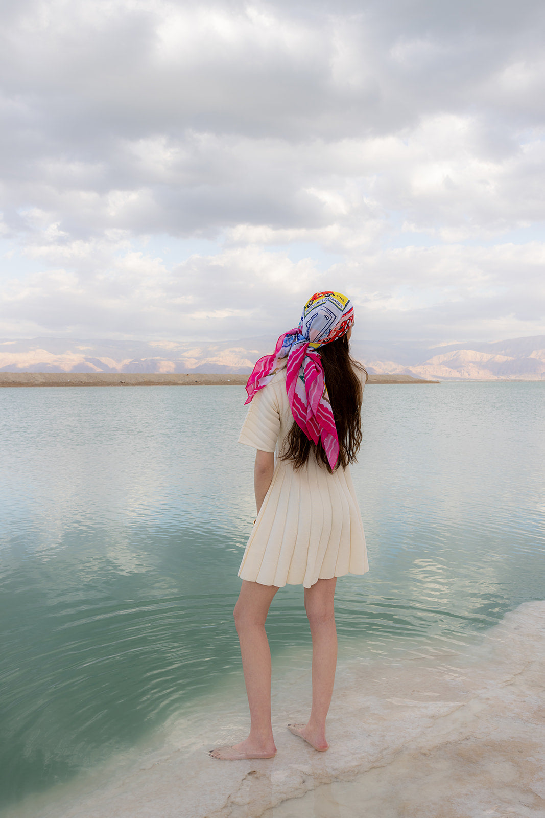 TUK Return To Sender Head Scarf worn by the sea, showcasing a colorful vintage postage stamp print silk head scarf.