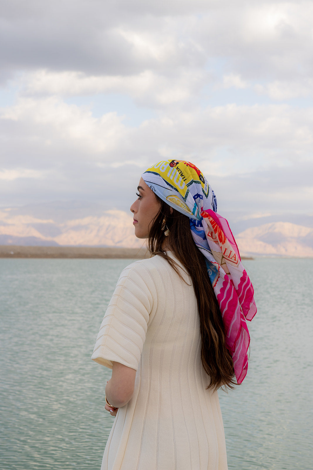 TUK Return To Sender Head Scarf styled by the sea, featuring a colorful vintage postage stamp print silk head scarf design.