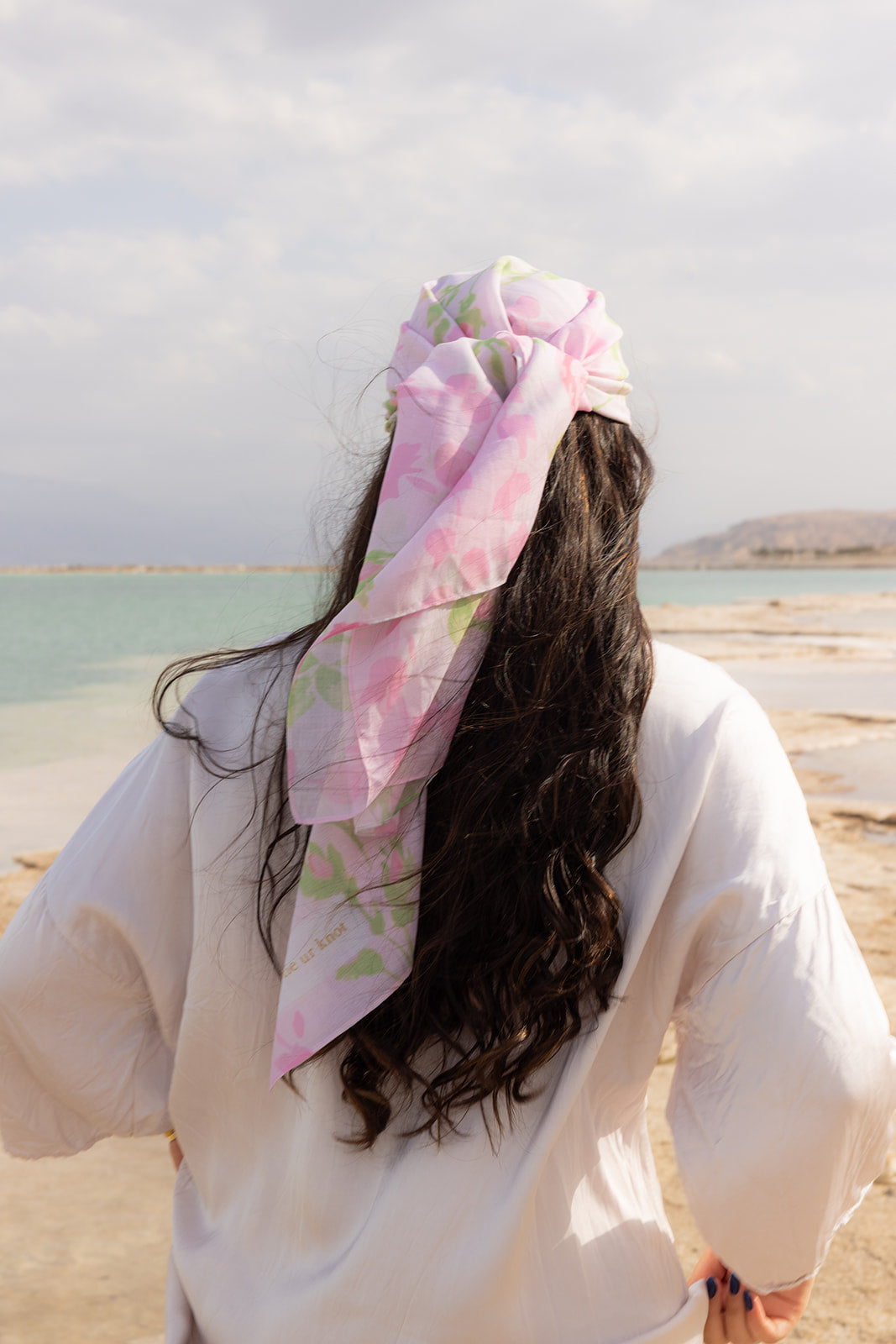 Rose To The Occasion Head Scarf by Tie Ur Knot featuring a soft pink floral print, styled elegantly by the seaside.