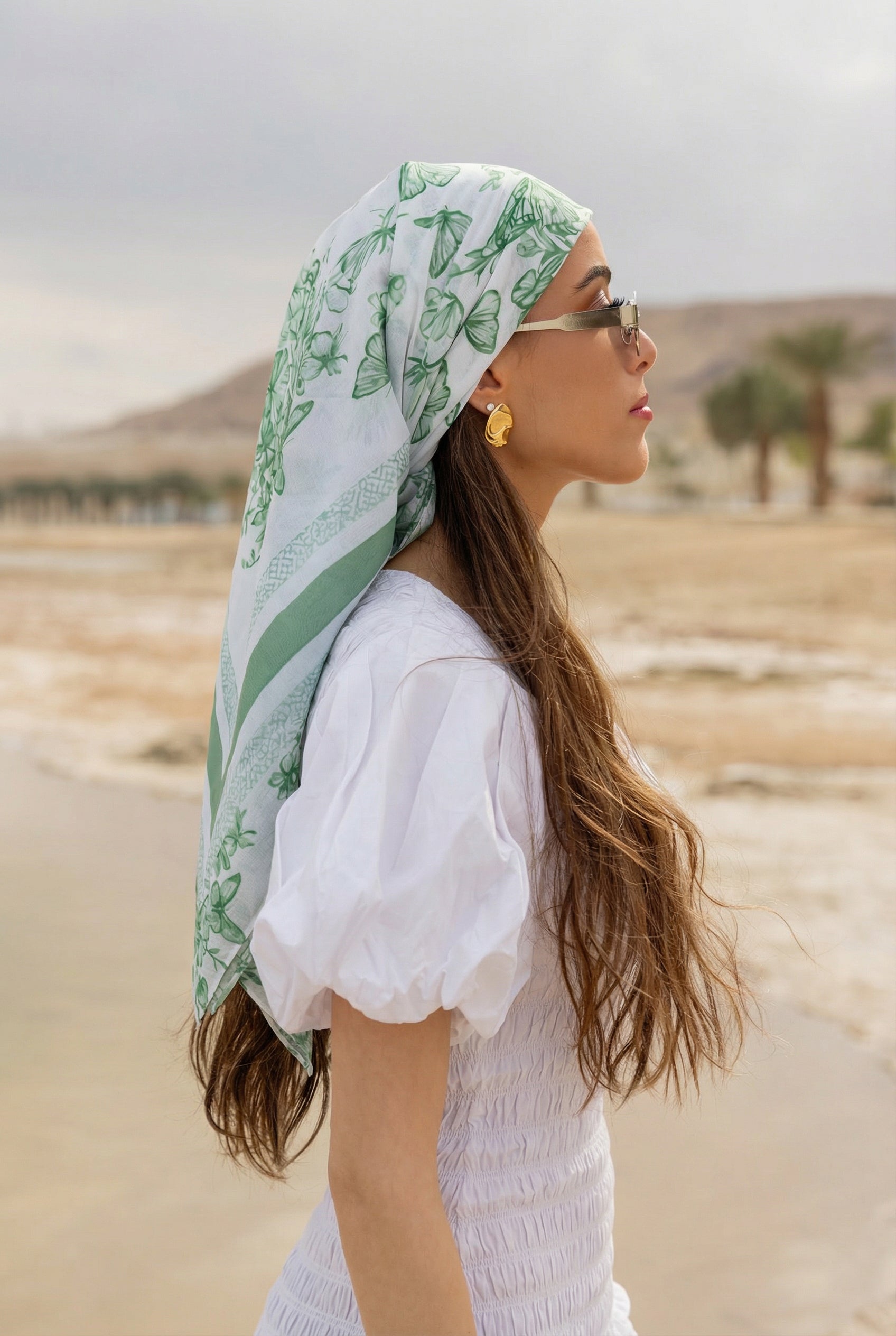 Woman in profile wearing TUK Sage Advice headscarf, green floral print modest fashion accessory styled in a neutral desert setting.