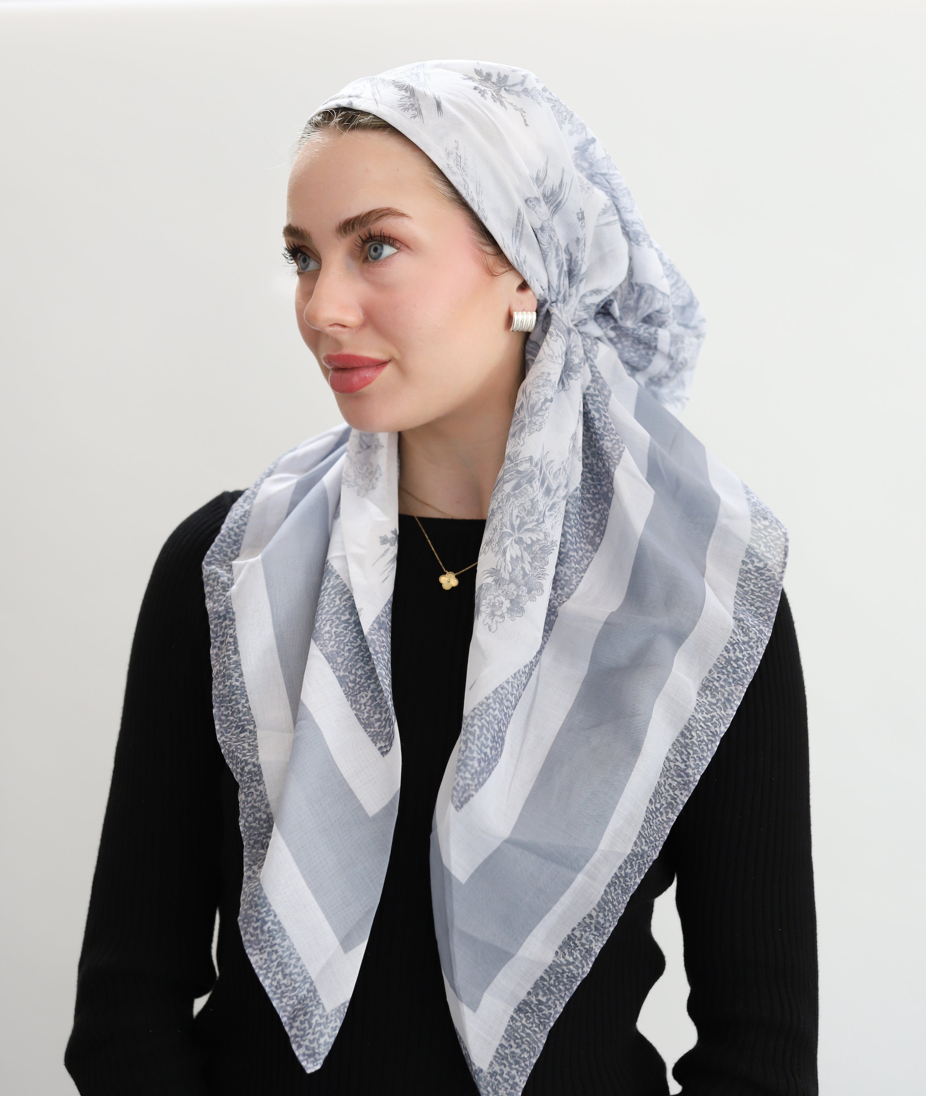 Woman wearing a white and gray patterned headscarf on a plain background