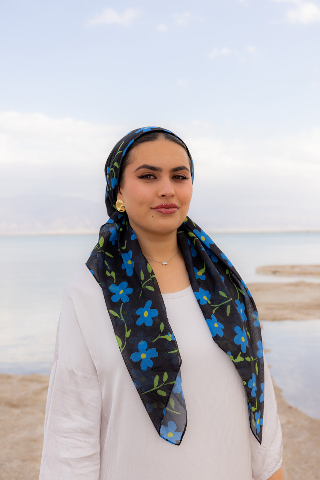 TUK Something Blue Head Scarf crochet bandana with blue floral print, styled by a woman in a coastal outdoor setting.