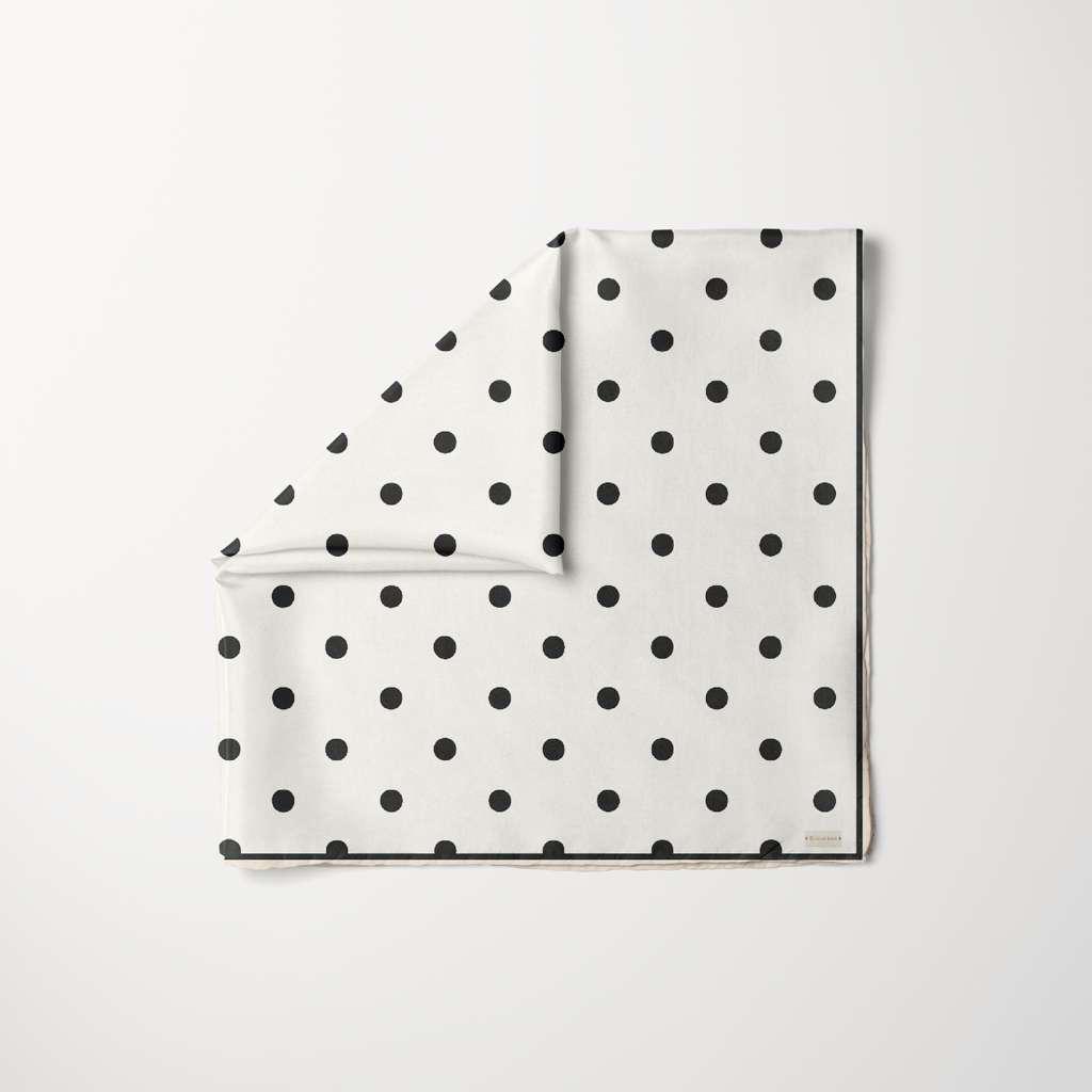 TUK Spot-On Scarf featuring a soft neutral base with minimalist black polka dot pattern, styled as a folded square scarf.
