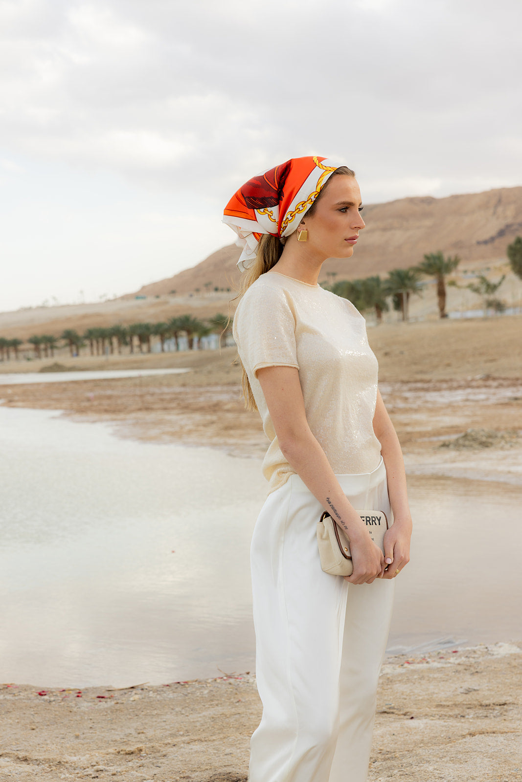 TUK Stirrup Society Silk Bandana with bold equestrian chain print styled as a silk headscarf by the waterfront outdoors.