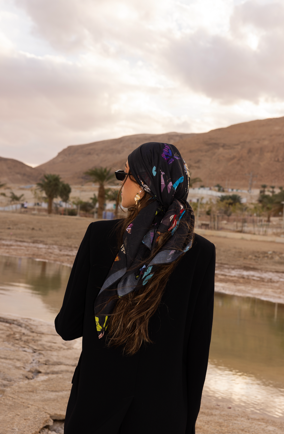 Woman wearing TUK The Night Shift headscarf, black butterfly print scarf styled outdoors in desert landscape, chic modest fashion.