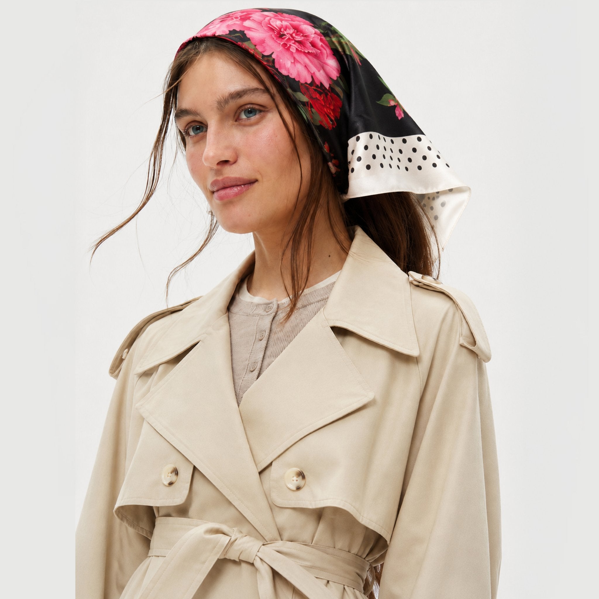 In Full Swing Silk Bandana worn by a woman with a trench coat. It is black with pink flowers.