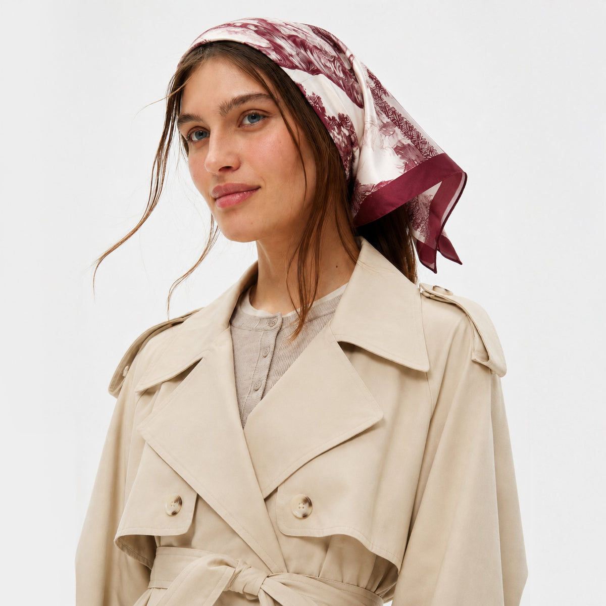 Untamed & Untied Silk Bandana in crimson and cream, styled as a headscarf on a woman with a beige trench coat